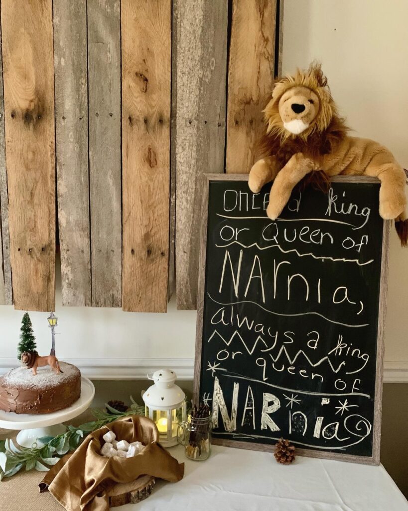 Chronicles of Narnia quote chalk on blackboard "Once a king or queen of Narnia, always a king or queen of Narnia" with Turkish delight, lantern and Aslan birthday cake with lamppost, tree and snow