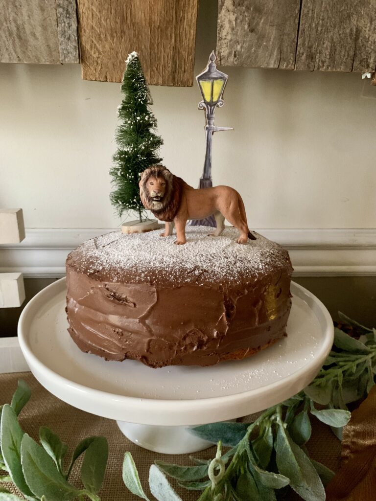 Chronicles of Narnia birthday cake with Aslan the lion, lamppost and tree on chocolate cake sprinkled with powdered sugar to represent snow