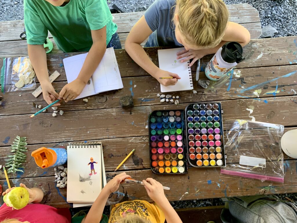 Colorful picture showing homeschool family nature journaling at a picnic table outside loving homeschooling