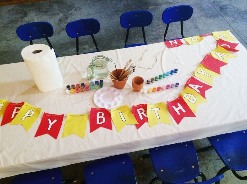 Winnie the Pooh birthday banner lying on craft table with chairs surrounding, paints and paintbrushes