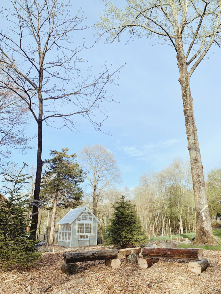 log benches in front of greenhouse and trees
