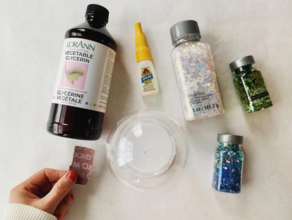 DIY snow globe supplies on table with glue, glitter, glycerin and plastic snow globe