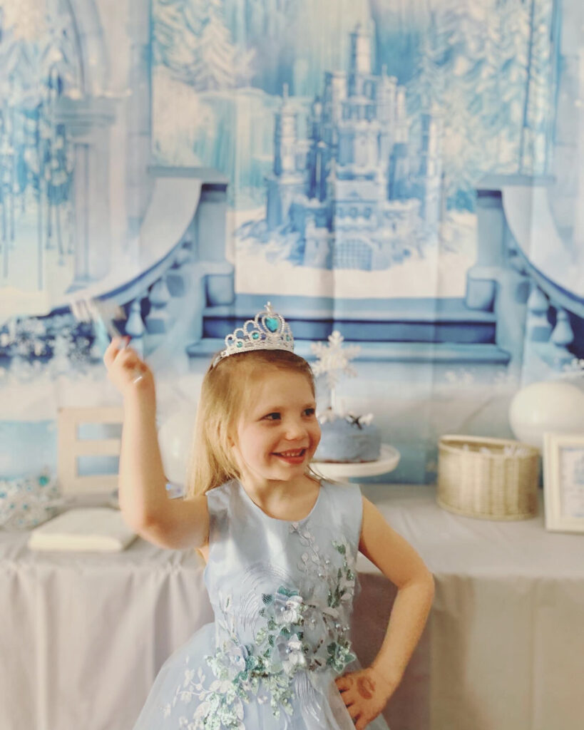 winter princess birthday girl in front of frozen palace backdrop snowflake wand and arctic animal cake