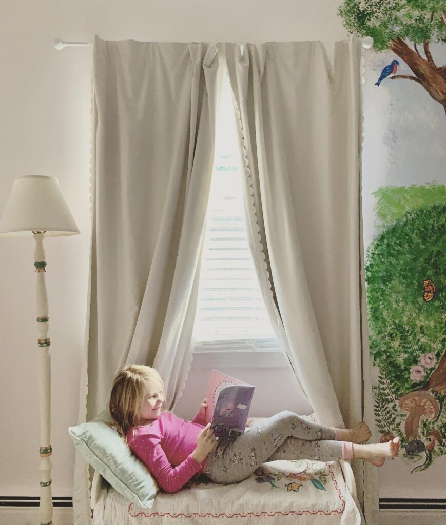 little girl reading in bedroom with woodland animal mural