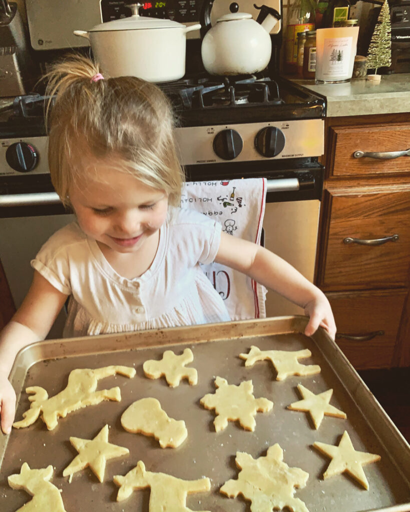 little girl holding baking sheet of ultimate fool-proof sugar cookie recipe at Christmas