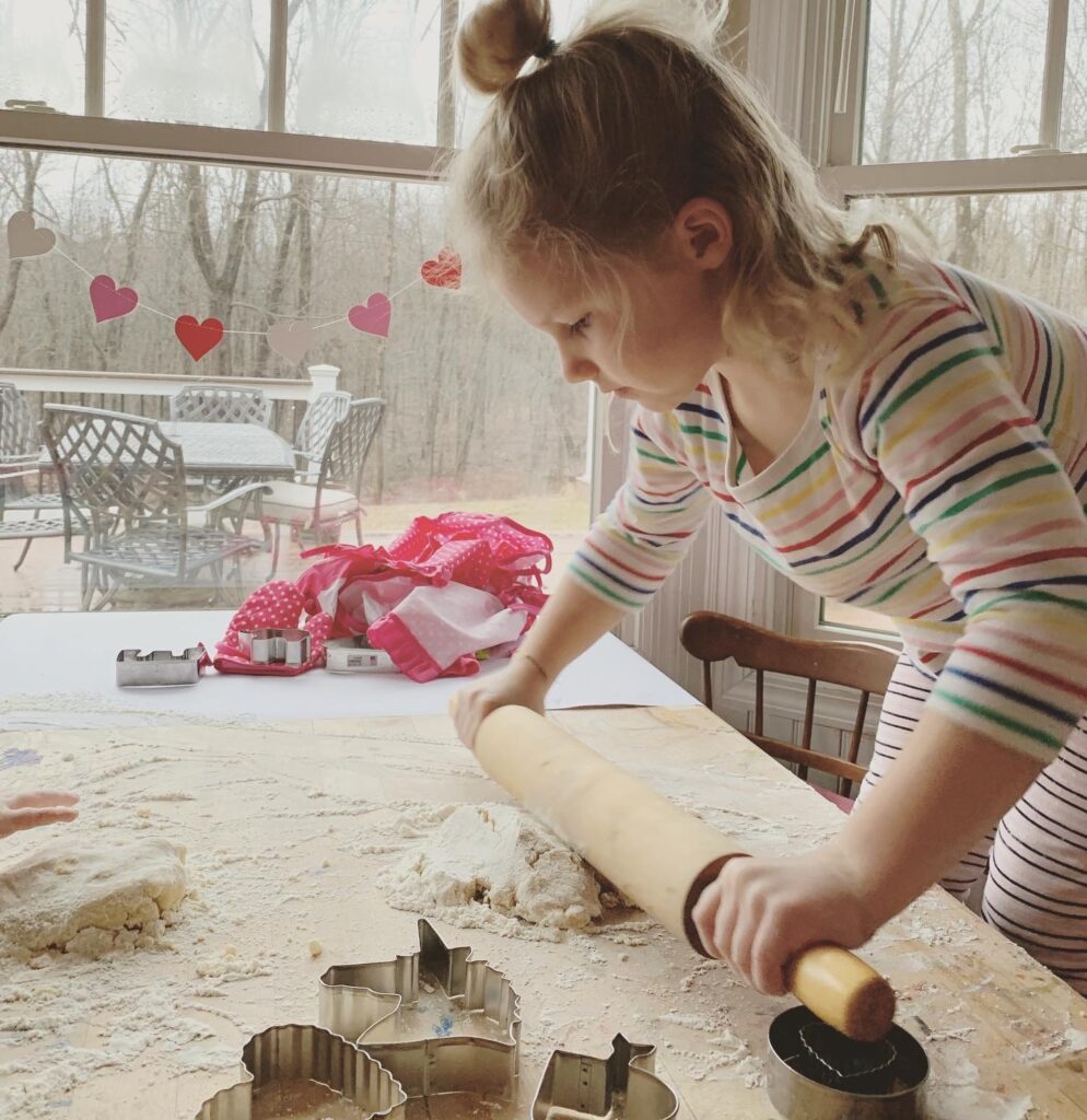 little girl rolling out ultimate fool-proof sugar cookie recipe on table with dough and flour