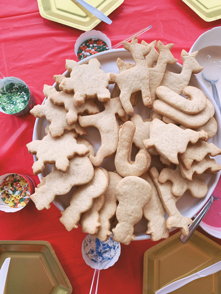 Christmas sugar cookies on plate with sprinkles for decorating on red tablecloth