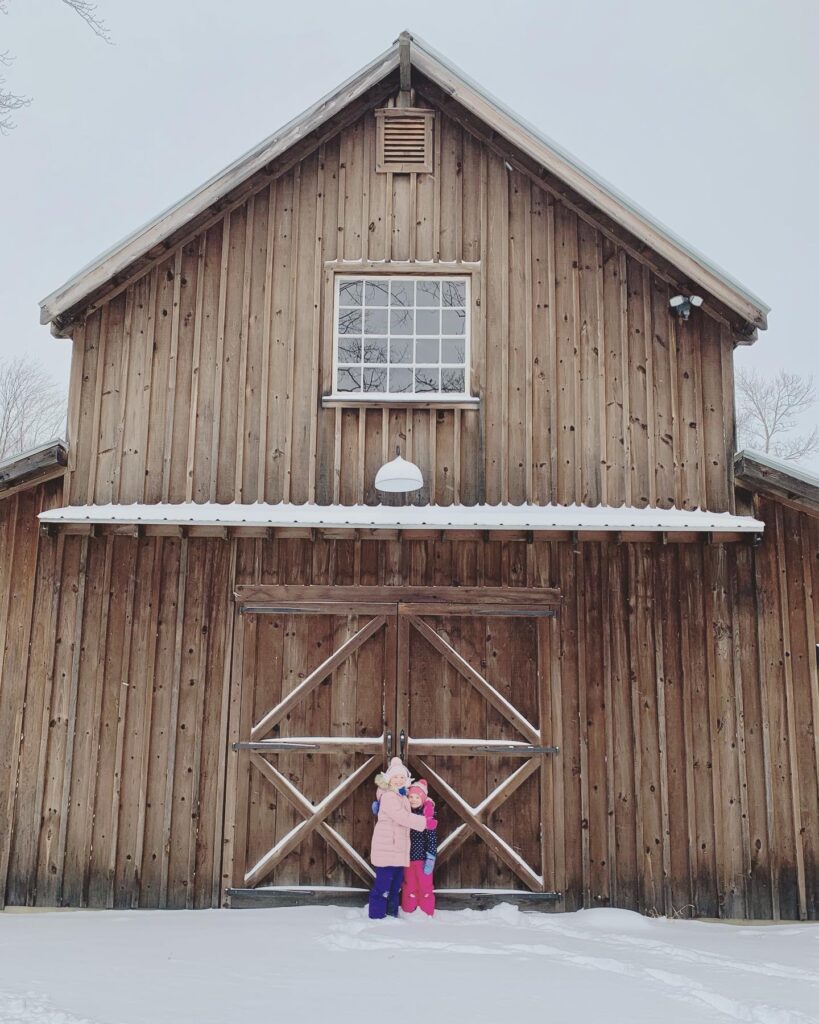 joy-filled kids in front of post and beam barn in snow