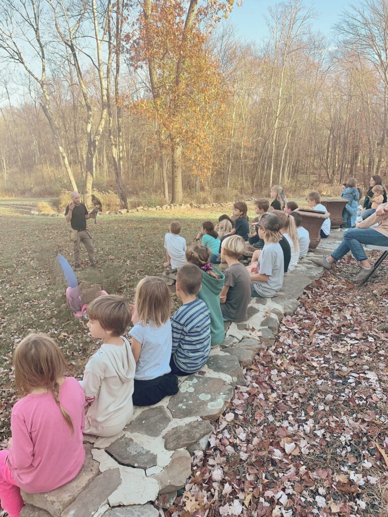 Falconer presentation in front of lots of kids sitting on rock wall outside