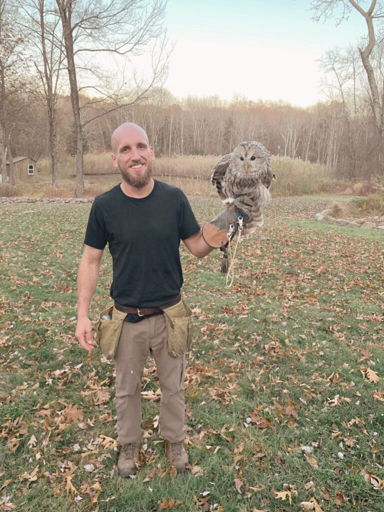 Falconer holding Owl in front of pond scene