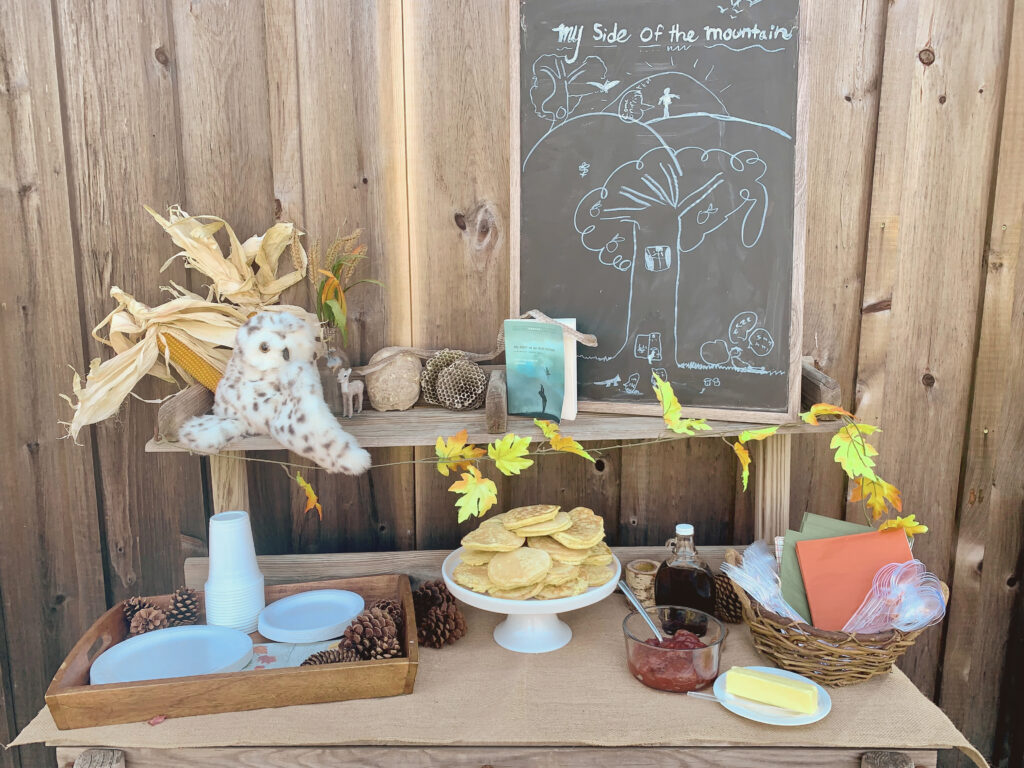 My Side of the Mountain Book Club table with pancakes, maple syrup, pinecones, paper plates, utensils