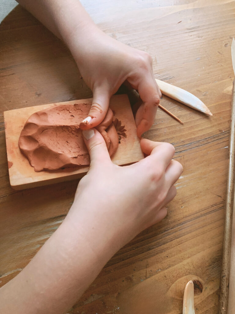 fingers pressing terra cotta clay into mold